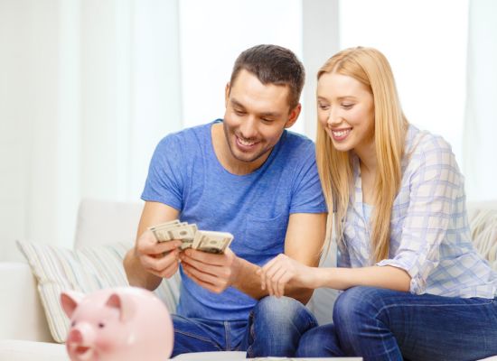 love, family, finance, money and happiness concpet - smiling couple counting money with piggybank ot table at home
