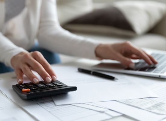 Close up of woman busy paying bills online on computer calculating household finances or taxes on machine, female manage home family expenditures, using calculator, make payment on laptop