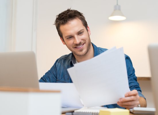 Happy young businessman reading paperwork at desk in office