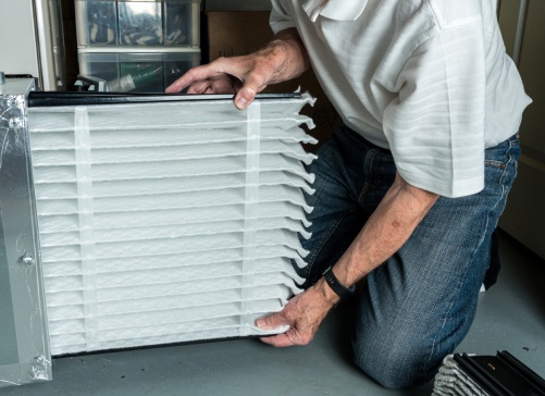 Senior caucasian man checking a clean folded air filter in the HVAC furnace system in basement of home