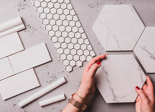 An individual displays a marble tile and a white tile, highlighting key material options for custom homes in Brownsville, TX.
