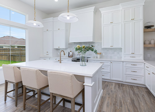 A luxurious white kitchen featuring a central island with bar stools, showcasing modern design and elegant upgrades.