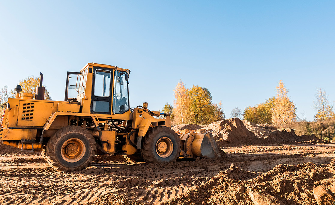 A yellow bulldozer navigates a dirt road, representing opportunities to buy land or construct a new home.